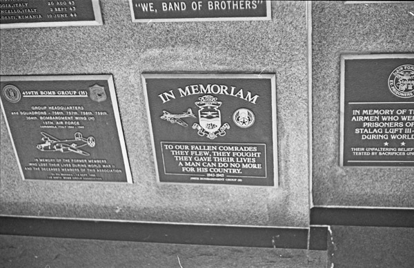A close-up of a series of memorial plaques.  The central one appears to have one above and to the left of it.