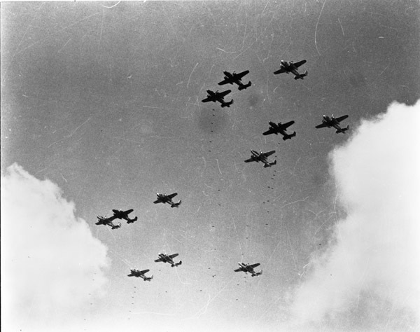 A ground view looking up at a dozen bombing planes flying through the sky.