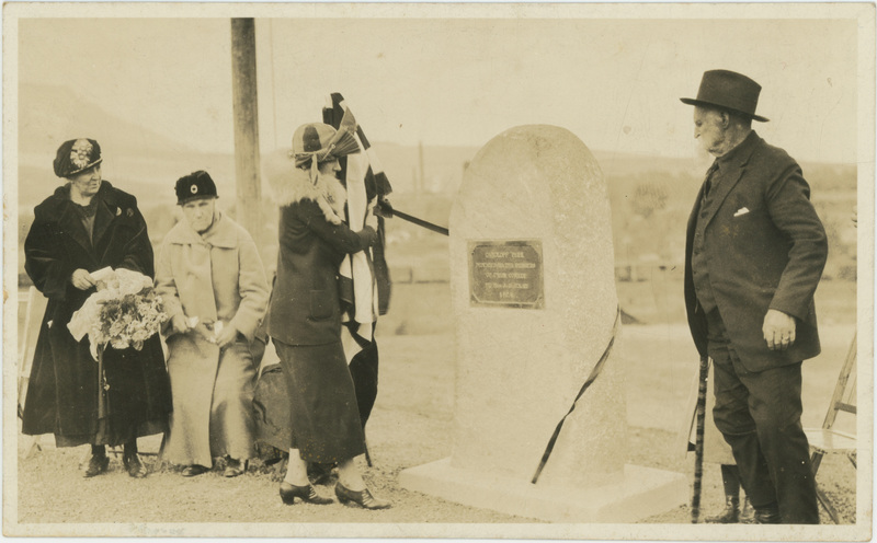 A group of three women standing on the left a dedication plaque, while a man stands to the right of it.