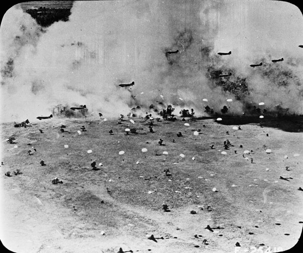 Multiple planes dropping paratroopers to the ground amidst a smoky sky.  