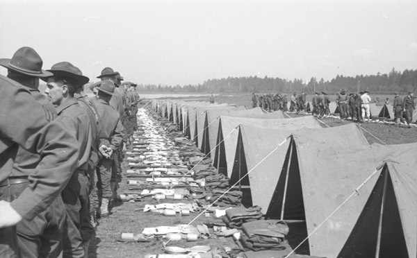 A line of soldiers with their backs to a line of tents, apparently preparing for inspection.  In front of the tents are neatly organized groups of equipment, most likely the contents of the tent and the soldiers' belongings.