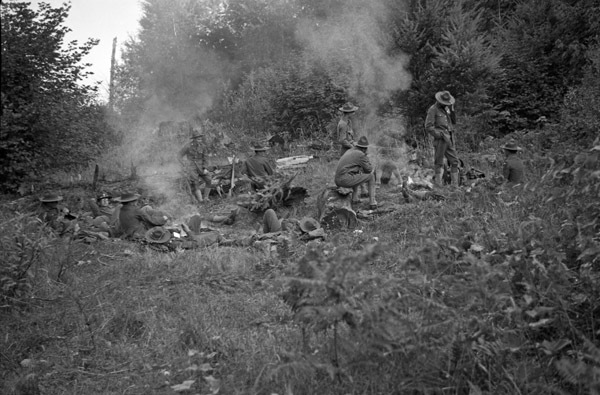 About a dozen soldiers sit around two campfires in relaxed positions.  They are in a clearing surrounded by woods.