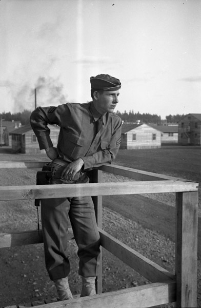A soldier leaning on their elbow on a railed wooden platform and looking off into the distance.