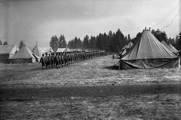 A long line of over a hundred soldiers walking away in formation from the camera angle through a large path in a tent camp.