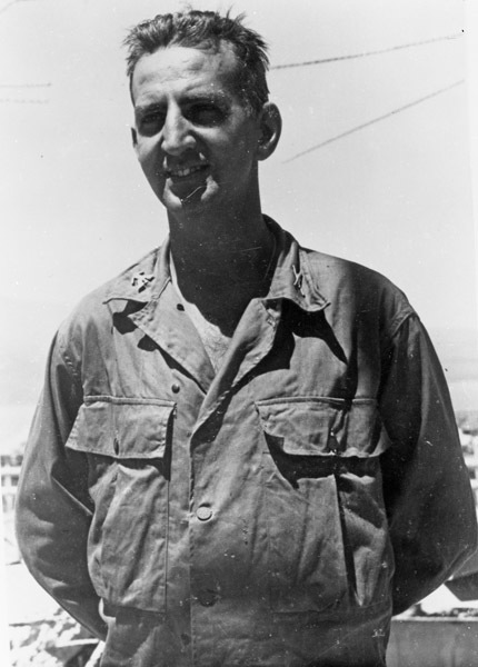 A soldier in unmarked fatigues standing and smiling at the camera.