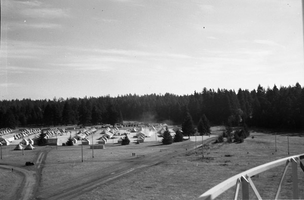 A semi-permanent military camp made up of many tents along a dirt road in a wooded clearing.