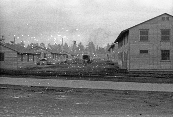 A road with two-story buildings on the right, and single-story buildings on the left. A truck is on the road, center of image.
