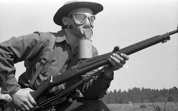A close up of a soldier with a gas mask on and holding a rifle.  He appears to be moving forward by his stance.