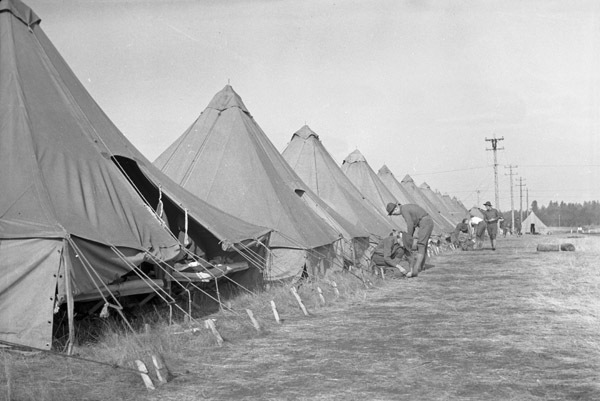 A semi-permanent military camp made up of many tents in a wooded clearing.  A few soldiers can be seen working or talking just outside of the tents.
