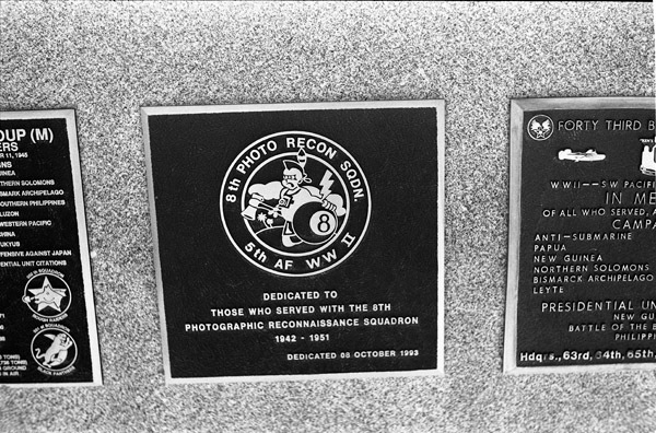 A close-up of a plaque set in a series of plaques. An image in the center shows a caricature of a Native American with a tomahawk in one hand and an eight-ball in the other. Other plaques can be seen to the left and right of the centered one. The caption is in the description.