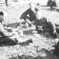 A group of four soldiers sitting and laying on the ground eating food. 