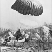 A paratrooper is just a foot off the ground and landing in his parachute.  Multiple other soldiers are nearby on the ground with their chutes still attached, probably having just landed.
