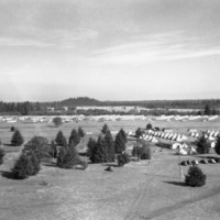 An view from on high and at a distance of a semi-permanent military camp in a wooded clearing.