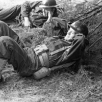 Two soldiers in full gear lay on the ground relaxing against some tree branches.  