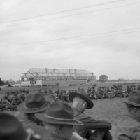 Soldiers sitting on the grass in a semicircle.  A few are seen holding rifles.