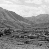A large military tent camp set in a low area surrounded by mountains.
