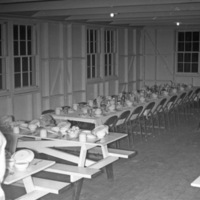 Tables in the mess hall with dirty dishes on them.  No one is at the tables.  One person is seen to the bottom left, facing away from the camera.