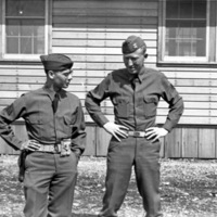 Two soldiers facing the camera and talking with one another, while having their hands on their hips in a relaxed pose.