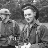 Three soldiers in uniforms standing in front of a tree line.  The center man is looking at the camera, while the others look in other directions.