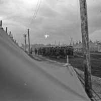 Rows of dozens of soldiers standing in formation in a large path surrounded by tents.  An officer is facing the formation.