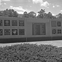 An outdoor memorial, with a central larger plaque and flanked by two sets of eight smaller plaques on both sides of the central one.