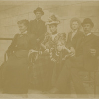 Three women, a man, sit for a posed photo, while two young boys stand in the background.