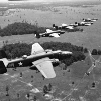 Five bombing planes flying over a sparsely forested grasslands, from the view of another airplane.