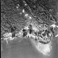 Bombs landing and exploding on a shoreline as seen from the air.