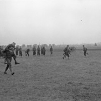 A small group of soldiers in a field giving other men piggy-back rides and smiling.  They appear to be racing, while other men look on the race.
