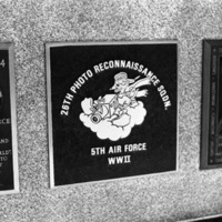 A close-up of a plaque set in a series of plaques.  Other plaques can be seen to the left and right of the centered one.  