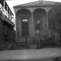 A soldier in dress uniform with their arm leaning on a fence in front of a single-level house. 
