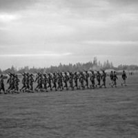 A couple dozen soldiers marching in formation with rifles resting on their shoulders.  A tent camp can be seen in the background.