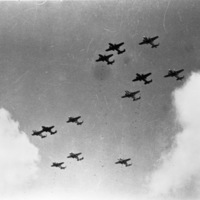 A ground view looking up at a dozen bombing planes flying through the sky.