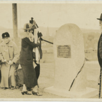 A group of three women standing on the left a dedication plaque, while a man stands to the right of it.