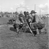 Three soldiers, each squatting down on one knee, huddled around a mortar.  A tented camp can be seen in the background.