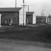 A line of two-story houses on the left, with a dirt road on the right.  Trees are in the background.