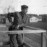 A soldier leaning on their elbow on a railed wooden platform and looking off into the distance.