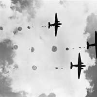Three military planes in the sky as seen from directly below.  There are numerous paratroopers in the sky behind the planes in various stages of deploying their parachutes.