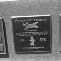 A close-up of a plaque set in a series of plaques.  Other plaques can be seen to the left and right of the centered one. 