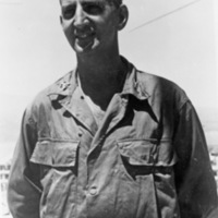 A soldier in unmarked fatigues standing and smiling at the camera.