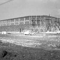A building under mostly complete construction, with scaffolding on the nearest side.  Two care are parked in the foreground.