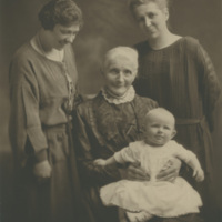 Two women standing around an older woman holding a baby girl in her lap.