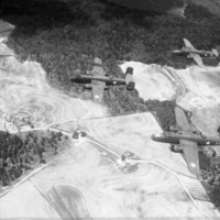 Five bombing planes flying over a moderately forested grasslands, from the view of another airplane.