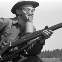 A close up of a soldier with a gas mask on and holding a rifle.  He appears to be moving forward by his stance.