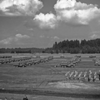 An elevated landscape view of military trucks and soldiers in lines in a wooded clearing. 