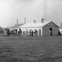 A couple dozen men working on a building that is nearly complete.  Two men stand on the roof, while the rest work on the ground.
