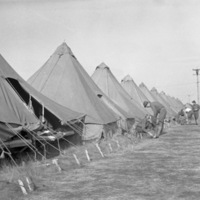 A semi-permanent military camp made up of many tents in a wooded clearing.  A few soldiers can be seen working or talking just outside of the tents.