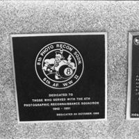 A close-up of a plaque set in a series of plaques.  An image in the center shows a caricature of a Native American with a tomahawk in one hand and an eight-ball in the other.  Other plaques can be seen to the left and right of the centered one.  The caption is in the description.