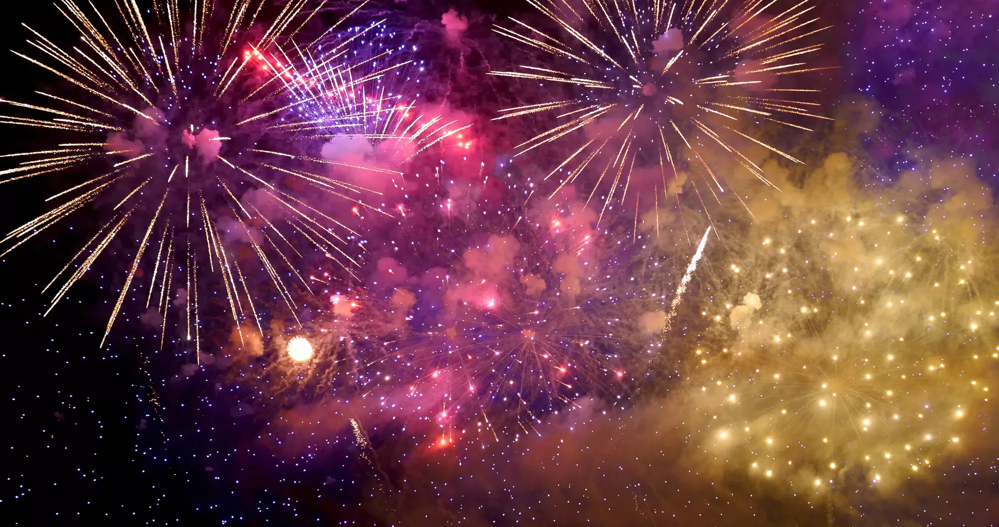 Spectacular fireworks display lighting up the night sky with vibrant bursts of gold, purple, and pink colors during a celebration