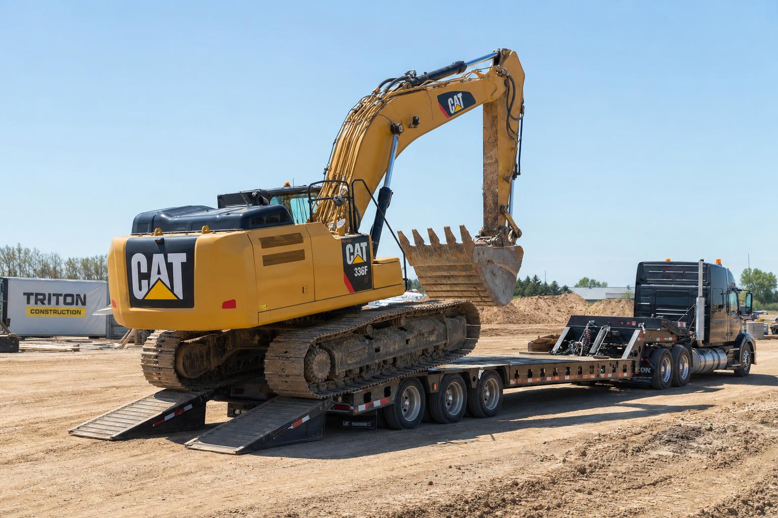 CAT 336F excavator loaded on a lowboy trailer at a Triton Construction job site on a sunny day